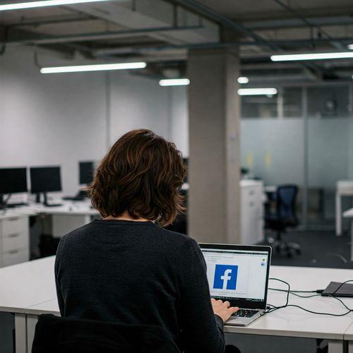 Această imagine prezintă o persoană concentrată, lucrând la un laptop într-un birou modern. Pe ecranul laptopului se distinge logo-ul Facebook, sugerând activități legate de social media sau marketing. Decorul biroului este minimalist și elegant, cu tonuri neutre și lumină naturală, creând o atmosferă profesională și confortabilă. Imaginea surprinde un moment de muncă dedicată, evidențiind importanța strategiei digitale în creșterea vânzărilor pe Facebook.